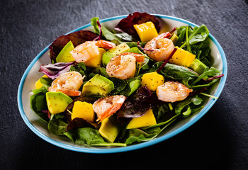 Salad with shrimps on black stone plate