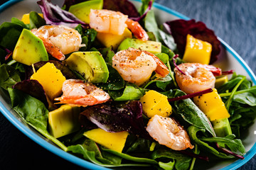 Salad with shrimps on black stone plate