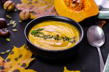 pumpkin cream soup with dark bread croutons and seeds with autumn leaves decoration on black background