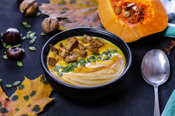 pumpkin cream soup with dark bread croutons and seeds with autumn leaves decoration on black background