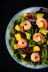 Salad with shrimps on black stone plate