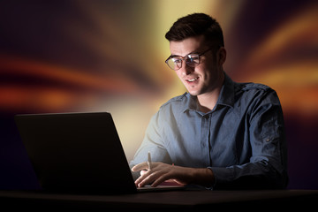 Young handsome businessman working late at night in the office with warm lights in the background