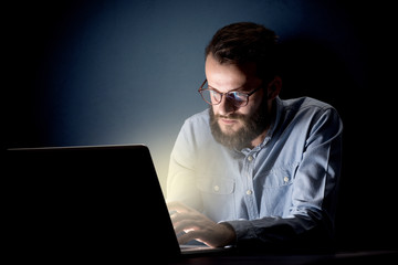 Young handsome businessman working late at night in the office with a dark background