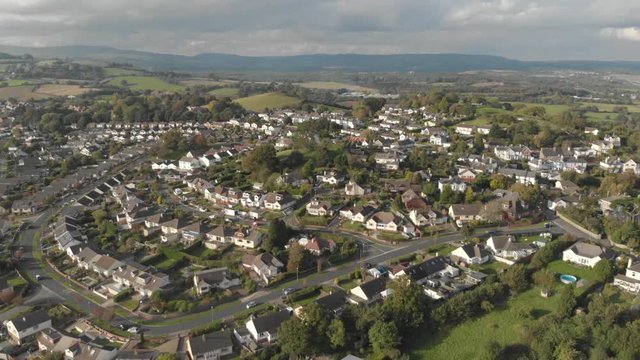 Residential streets in town, surrounded by green fields & countryside, rising drone shot