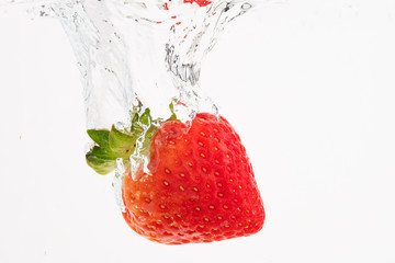 Fresh strawberry dropped into crystal clear water with splash isolated on white background