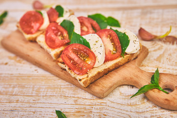Caprese bruschetta toasts on a cutting board. Bruschetta with tomatoes, mozzarella cheese and basil on a rustic table. Traditional italian appetizer or snack, antipasto