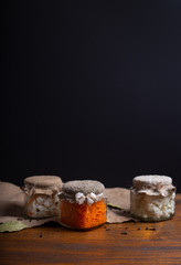 Sauerkrau, cauliflower and pickled carrot in the canning jars on the wood table with dark background. Decorated with  pepper and bay leaf. Fermented vegetables. Salad with pickled cabbage. Copy space.
