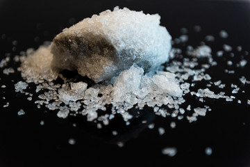 Large crystal of salt on black reflective surface; selective focus; natural edible salt