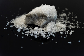 Large crystal of salt on black reflective surface; selective focus; natural edible salt
