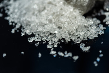 Large crystal of salt on black reflective surface; selective focus; natural edible salt