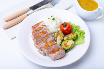 Grilled duck with mashed cauliflower, fried brussels sprouts and orange sauce on a white plate. Close-up.