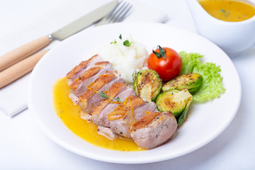 Grilled duck with mashed cauliflower, fried brussels sprouts and orange sauce on a white plate. Close-up.