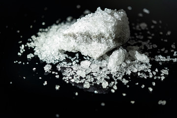 Large crystal of salt on black reflective surface; selective focus; natural edible salt