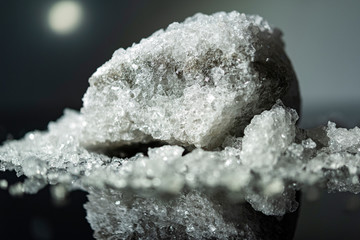Large crystal of salt on black reflective surface; selective focus; natural edible salt