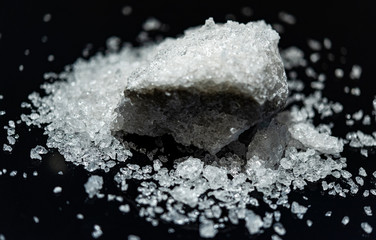 Large crystal of salt on black reflective surface; selective focus; natural edible salt