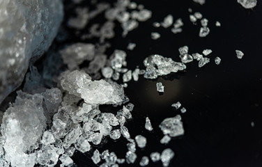 Large crystal of salt on black reflective surface; selective focus; natural edible salt
