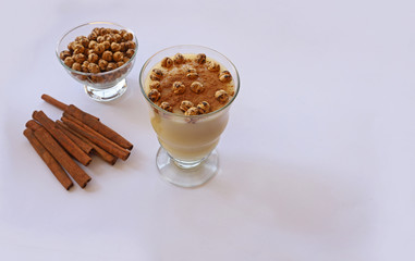 Boza in glass and lebelebi on it and cinnamon next to leblebi in bowl.