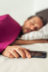 Sleeping young handsome man while holding his mobile phone. Screen on the phone is turned off