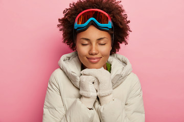Feeling reaxed and happy. Healthy adorable woman with curly hair, wears white down padded coat and...
