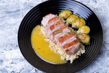 Grilled duck with fried Brussels sprouts, rice from cauliflower and orange sauce on a black plate. Close-up, selective focus.