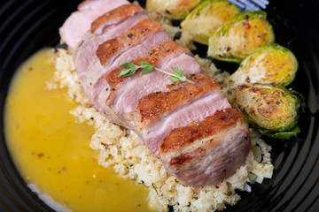 Grilled duck with fried Brussels sprouts, rice from cauliflower and orange sauce on a black plate. Close-up, selective focus.