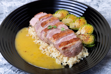 Grilled duck with fried Brussels sprouts, rice from cauliflower and orange sauce on a black plate. Close-up, selective focus.