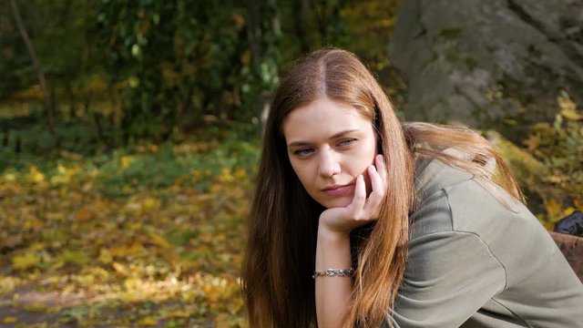Young beautiful sad woman is sitting on a bench in autumn park.