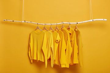 Collection of plain yellow sweaters and jackets for women hanging on rack in dressing room....