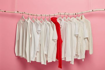 Ladies white casual clothes arranged on hangers, red knitted warm sweater stands out of whole collection. Dressing set hanging against pink background. Home wardrobe. Classic style. Fashion shop