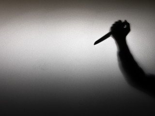 Halloween concept. Blurred shadow of hand holding sharp knife behind white mirror background....