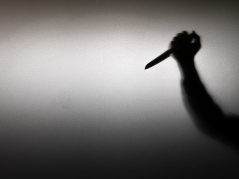 Halloween concept. Blurred shadow of hand holding sharp knife behind white mirror background. Murder scene.