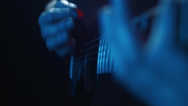 Guitarist playing acoustic guitar, lit by eerie blue lights