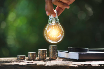Hand of male holding a light bulb with stack of coins and copy space for accounting, ideas and creative concept.