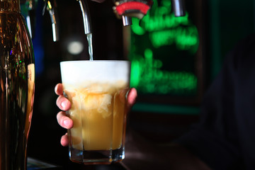 The bartender pours beer into a large glass in a restaurant. Photo without a face.