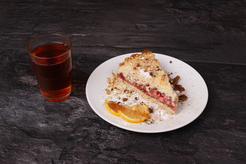 Shortcake and lemon in a white plate and tea in a glass cup on a towel on a dark background