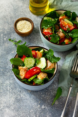 Tasty and healthy Salmon Grilled Salad with cucumber, tomatoes, fresh arugula and sesame seeds on a gray stone table. Free space for your text.