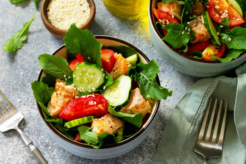 Tasty and healthy Salmon Grilled Salad with cucumber, tomatoes, fresh arugula and sesame seeds on a gray stone table.