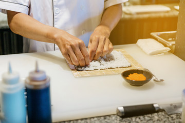 Obraz na płótnie Canvas Chef prepare to rolling Maki Sushi with Rice and Shrimp Tempura by adjust sushi rice with dry seaweed on sushi mat.