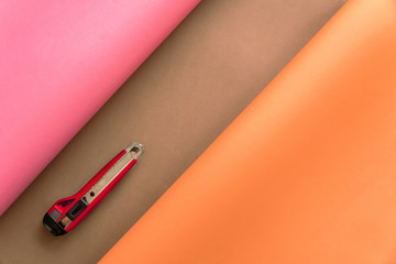 Pink and orange papers bending over brown color background in abstract form with red cutter....