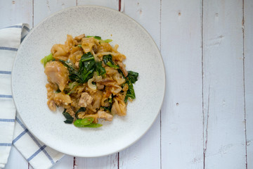 Stir fried flat noodle with Chinese kale, Soy sauce and pork in white dish.