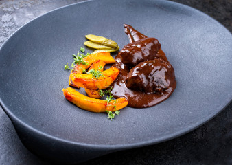 Traditional German braised beef cheeks in brown red wine sauce with pumpkin slices and herbs offered as closeup in a modern design plate
