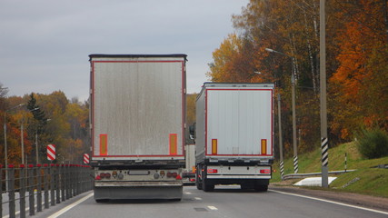 Trucks moving on autumn asphalt road, rear view on goods delivery cargo logistics