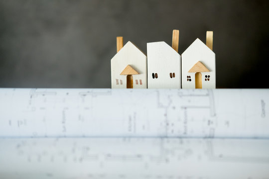 Miniature Home On Bunch Of Paper Rolled Up Building Plans