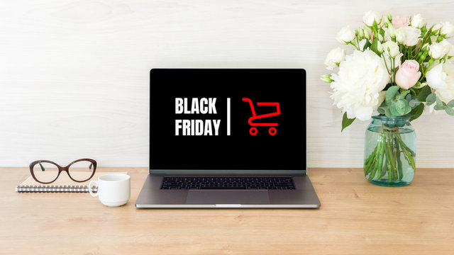 Black friday concept. Laptop computer screen with shopping card and sign "Black friday" on wooden desk