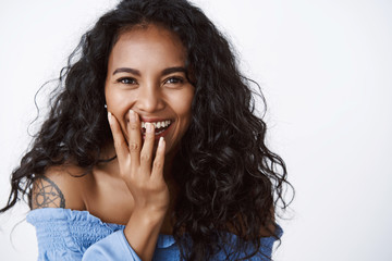 Fun, real emotions and women concept. Close-up attractive curly-haired feminine woman with tattoos in blue blouse, giggle cover smile with hand, enjoying funny party, standing white background