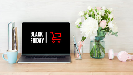 Black Friday concept. Laptop screen with text sign "Black Friday" and shopping cart on women workplace