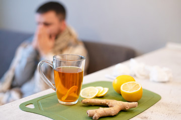 The concept of the disease, winter time. Black tea, lemon and ginger on the table, a sick man in the background, flu. Epidemic, sick leave, temperature, stress