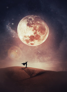 Surreal scene with a woman hero silhouette with cape on the top of a hill raises hand up to the sky watching the full moon night. Mystic night view.