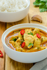 Spicy chicken breast in yellow curry sauce with garlic and chili  pepper with boiled rice in a bowl on a dark wooden background.
