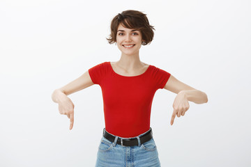 Motivated good-looking assertive cheerful young woman introduce promo pointing down index fingers...